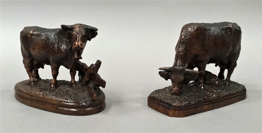 A pair of late nineteenth-century carved dark wood cows mounted on integrated plinths, showing textured coats and bells carved around their necks. View II