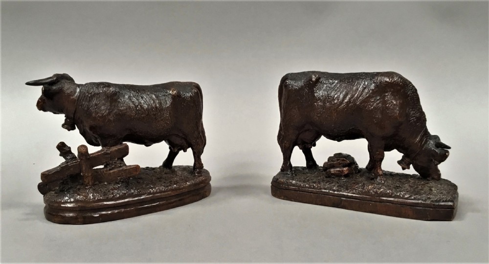 A pair of late nineteenth-century carved dark wood cows mounted on integrated plinths, showing textured coats and bells carved around their necks. View VII