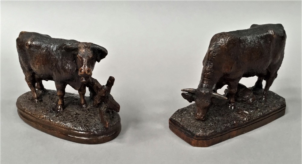 A pair of late nineteenth-century carved dark wood cows mounted on integrated plinths, showing textured coats and bells carved around their necks. View XII