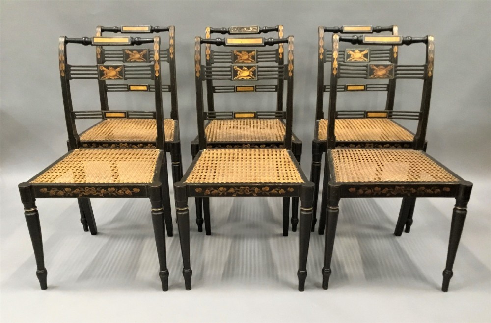 A set of six black-painted Regency side chairs featuring detailed parcel gilt decoration, horizontal slat backs, and natural woven cane seats. View II
