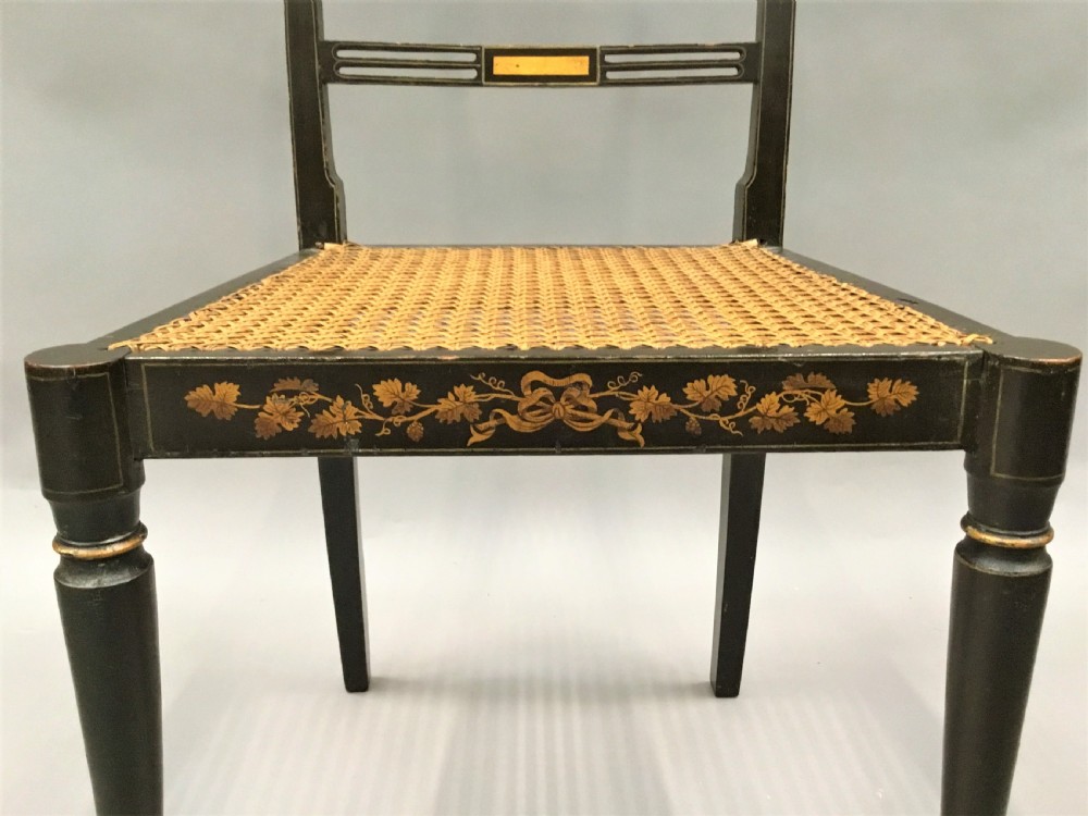 A set of six black-painted Regency side chairs featuring detailed parcel gilt decoration, horizontal slat backs, and natural woven cane seats. View XI