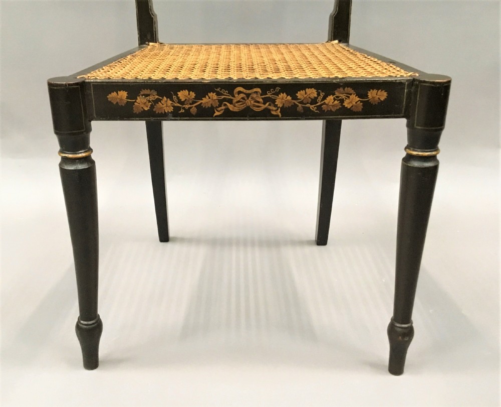 A set of six black-painted Regency side chairs featuring detailed parcel gilt decoration, horizontal slat backs, and natural woven cane seats. View XII