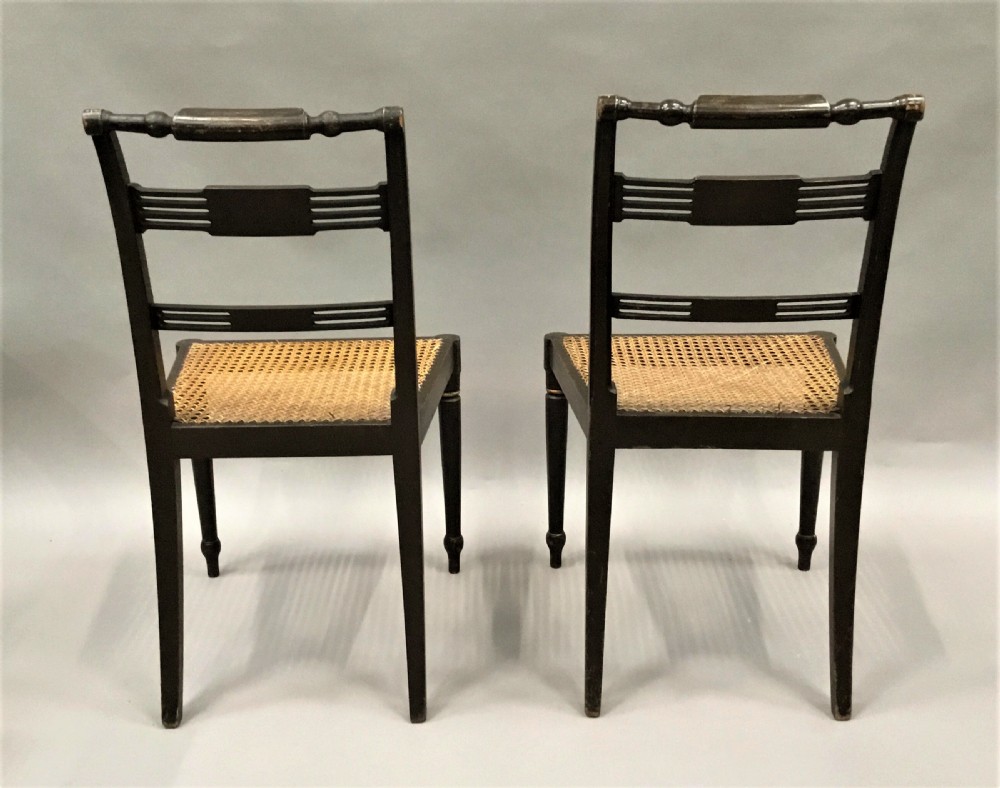 A set of six black-painted Regency side chairs featuring detailed parcel gilt decoration, horizontal slat backs, and natural woven cane seats. View XIV