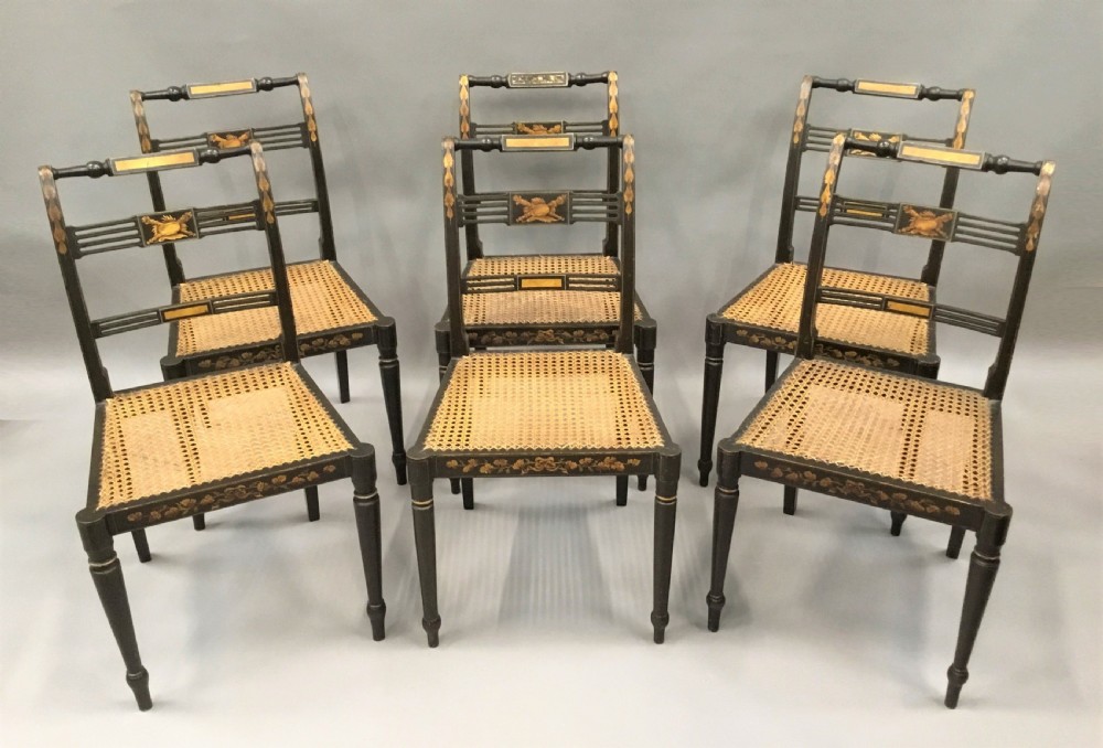 A set of six black-painted Regency side chairs featuring detailed parcel gilt decoration, horizontal slat backs, and natural woven cane seats. View XVI