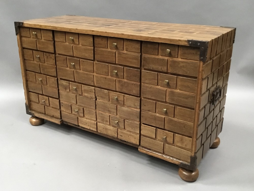 An 18th-century Spanish walnut low cabinet featuring a brick-patterned wooden facade, iron corner brackets, side handles, and multiple drawers with small brass knobs. View V