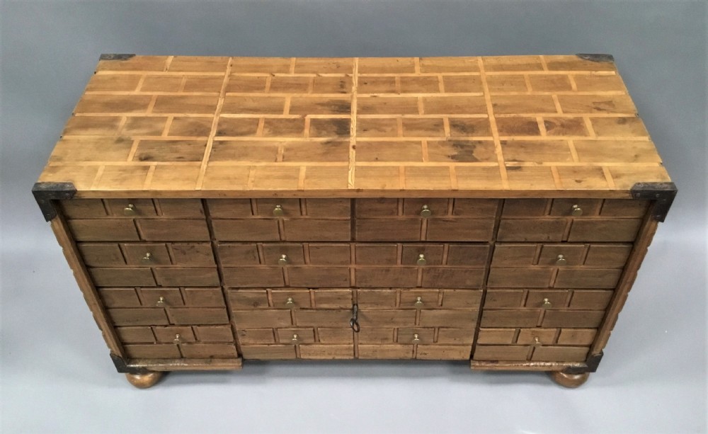 An 18th-century Spanish walnut low cabinet featuring a brick-patterned wooden facade, iron corner brackets, side handles, and multiple drawers with small brass knobs. View VI