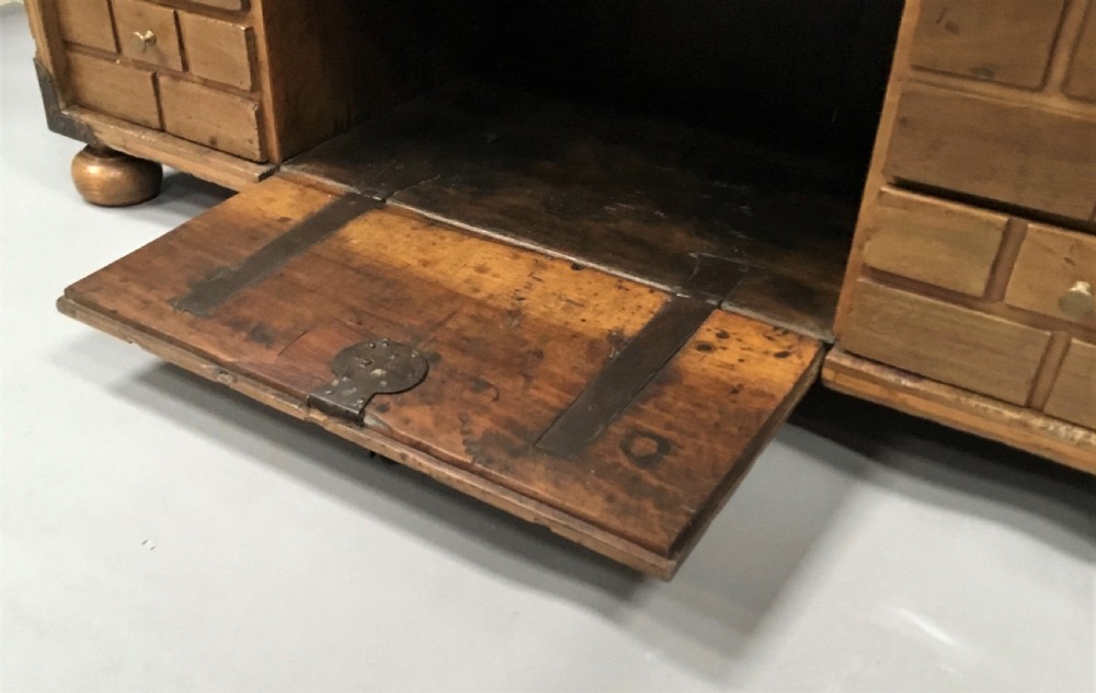 An 18th-century Spanish walnut low cabinet featuring a brick-patterned wooden facade, iron corner brackets, side handles, and multiple drawers with small brass knobs. View IX