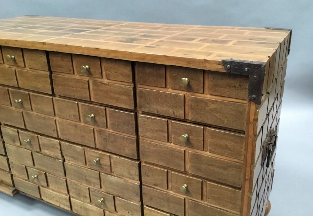 An 18th-century Spanish walnut low cabinet featuring a brick-patterned wooden facade, iron corner brackets, side handles, and multiple drawers with small brass knobs. View XVI