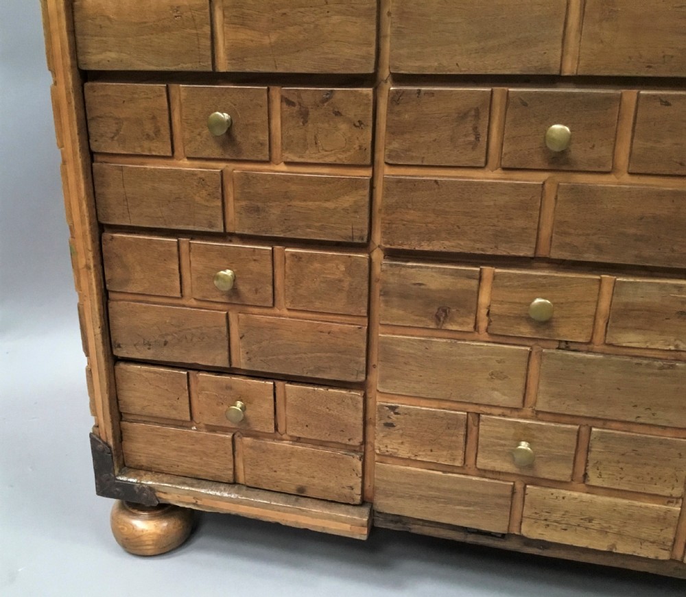 An 18th-century Spanish walnut low cabinet featuring a brick-patterned wooden facade, iron corner brackets, side handles, and multiple drawers with small brass knobs. View XVII