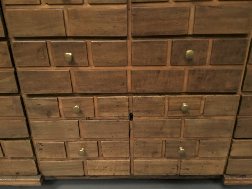 An 18th-century Spanish walnut low cabinet featuring a brick-patterned wooden facade, iron corner brackets, side handles, and multiple drawers with small brass knobs. View XVIII