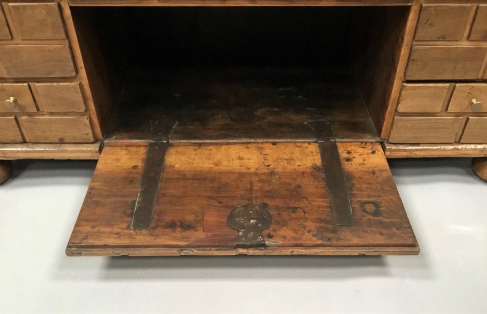 An 18th-century Spanish walnut low cabinet featuring a brick-patterned wooden facade, iron corner brackets, side handles, and multiple drawers with small brass knobs. View XIX