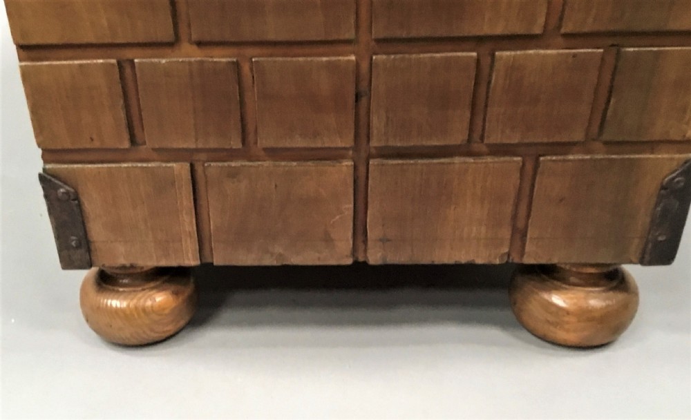 An 18th-century Spanish walnut low cabinet featuring a brick-patterned wooden facade, iron corner brackets, side handles, and multiple drawers with small brass knobs. View XXI