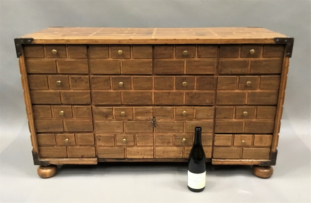 An 18th-century Spanish walnut low cabinet featuring a brick-patterned wooden facade, iron corner brackets, side handles, and multiple drawers with small brass knobs. View II