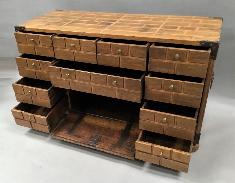 An 18th-century Spanish walnut low cabinet featuring a brick-patterned wooden facade, iron corner brackets, side handles, and multiple drawers with small brass knobs. View VIII
