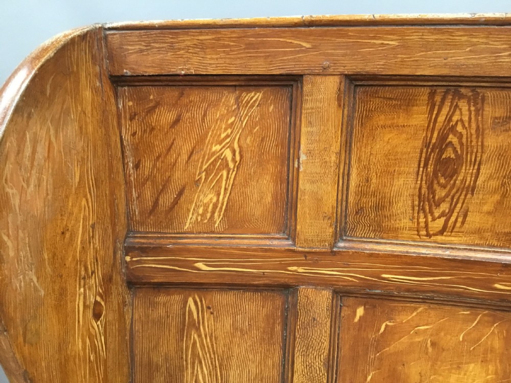 An antique Georgian high-backed wooden settle featuring a curved panelled back with a warm brown scumbled painted finish and integrated seat. View XIX