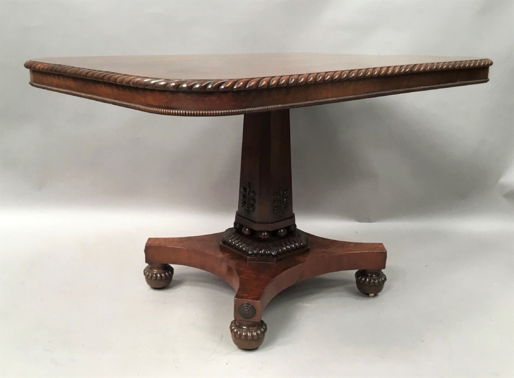 A Regency mahogany centre table featuring a rounded square top with rope-twist carved moulding, supported by a central tapered pedestal and a quadform base with lobed feet.