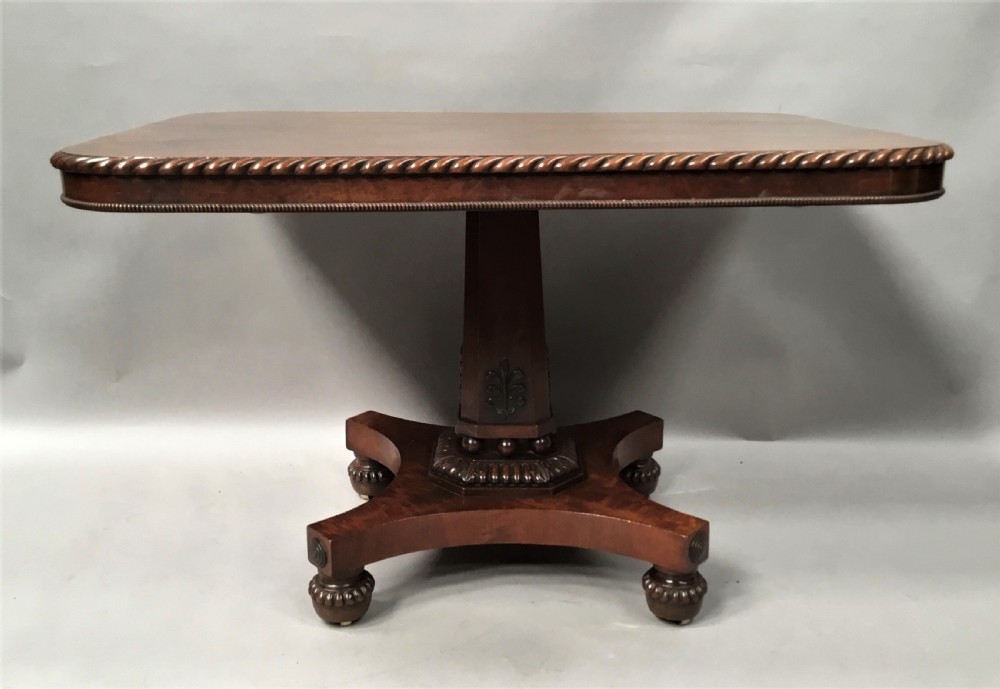 A Regency mahogany centre table featuring a rounded square top with rope-twist carved moulding, supported by a central tapered pedestal and a quadform base with lobed feet. View IV