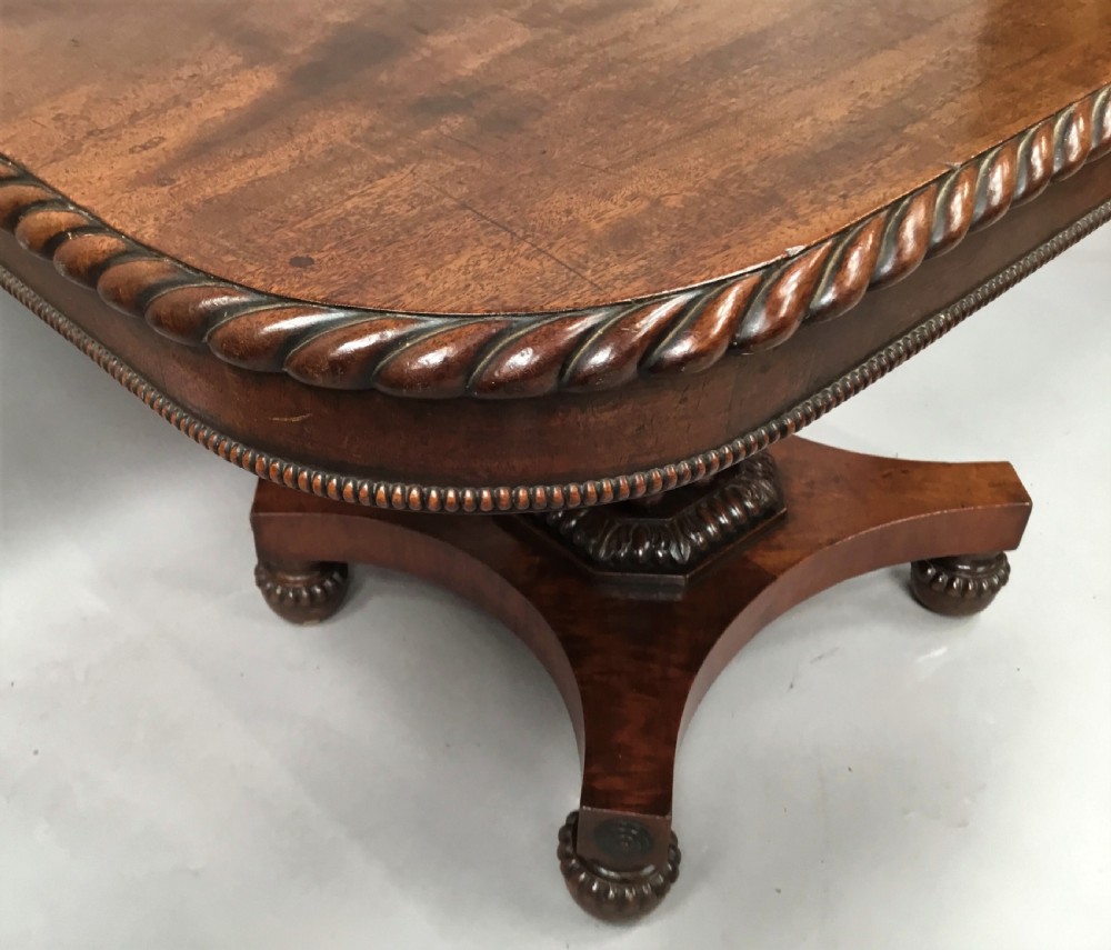 A Regency mahogany centre table featuring a rounded square top with rope-twist carved moulding, supported by a central tapered pedestal and a quadform base with lobed feet. View VI