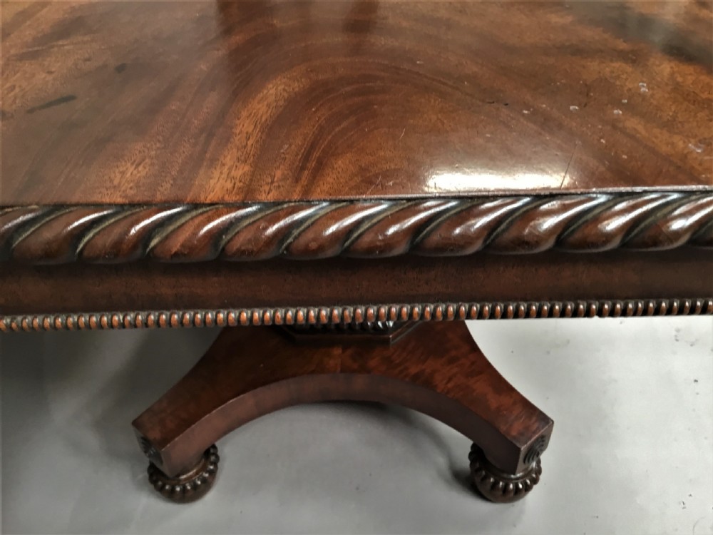 A Regency mahogany centre table featuring a rounded square top with rope-twist carved moulding, supported by a central tapered pedestal and a quadform base with lobed feet. View VII