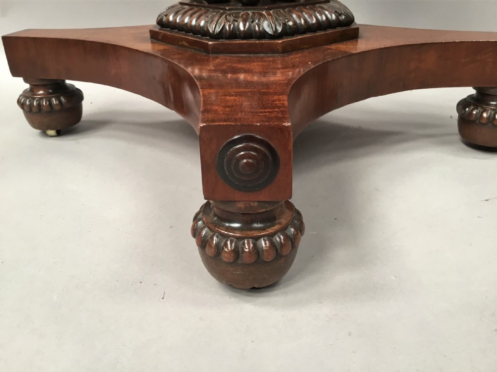 A Regency mahogany centre table featuring a rounded square top with rope-twist carved moulding, supported by a central tapered pedestal and a quadform base with lobed feet. View X