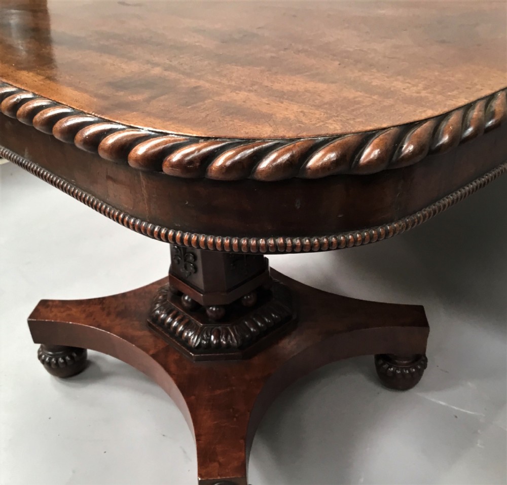 A Regency mahogany centre table featuring a rounded square top with rope-twist carved moulding, supported by a central tapered pedestal and a quadform base with lobed feet. View XV