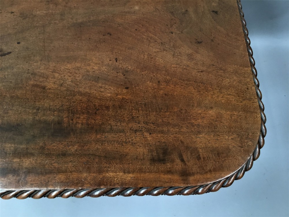 A Regency mahogany centre table featuring a rounded square top with rope-twist carved moulding, supported by a central tapered pedestal and a quadform base with lobed feet. View XVII