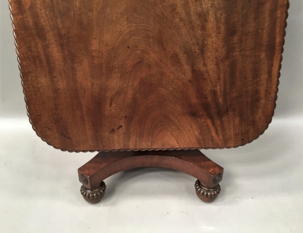 A Regency mahogany centre table featuring a rounded square top with rope-twist carved moulding, supported by a central tapered pedestal and a quadform base with lobed feet. View XIX