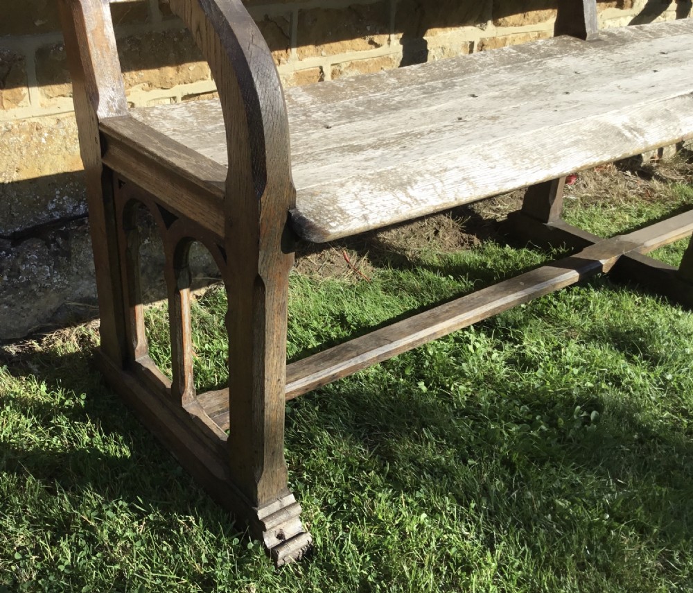 A 19th-century weathered oak orangery bench featuring a slatted back, carved finials, and Gothic-inspired side supports. View XIV