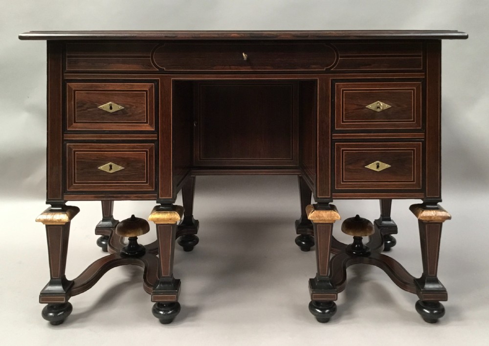 A 19th-century French rosewood kneehole desk featuring line inlay, brass escutcheons, a central recessed cupboard, and eight tapered legs connected by curved stretchers.