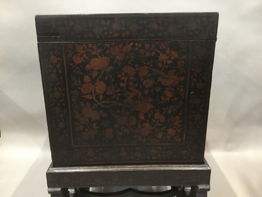 A dark brown rectangular lacquered wooden chest decorated with all-over floral pattern, set on a deeply carved scrolled wooden stand. View III