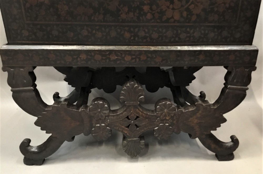 A dark brown rectangular lacquered wooden chest decorated with all-over floral pattern, set on a deeply carved scrolled wooden stand. View IV