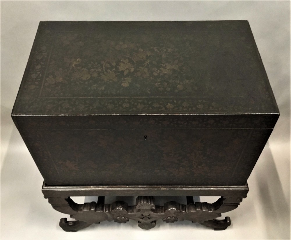 A dark brown rectangular lacquered wooden chest decorated with all-over floral pattern, set on a deeply carved scrolled wooden stand. View XIII