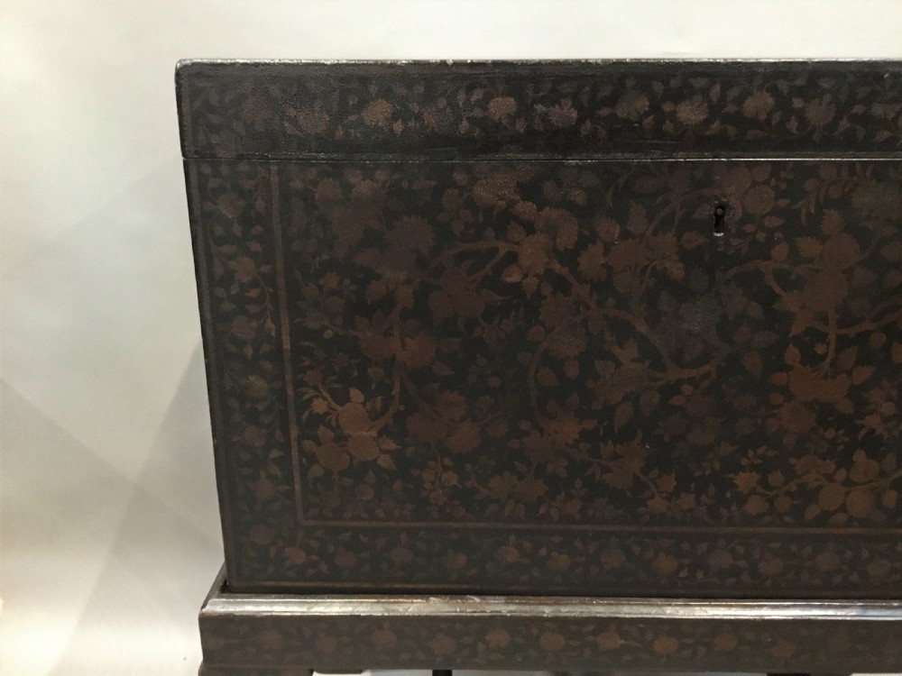 A dark brown rectangular lacquered wooden chest decorated with all-over floral pattern, set on a deeply carved scrolled wooden stand. View XV