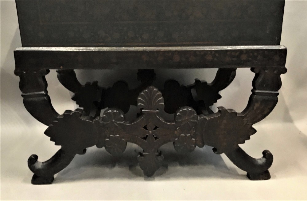 A dark brown rectangular lacquered wooden chest decorated with all-over floral pattern, set on a deeply carved scrolled wooden stand. View XVII