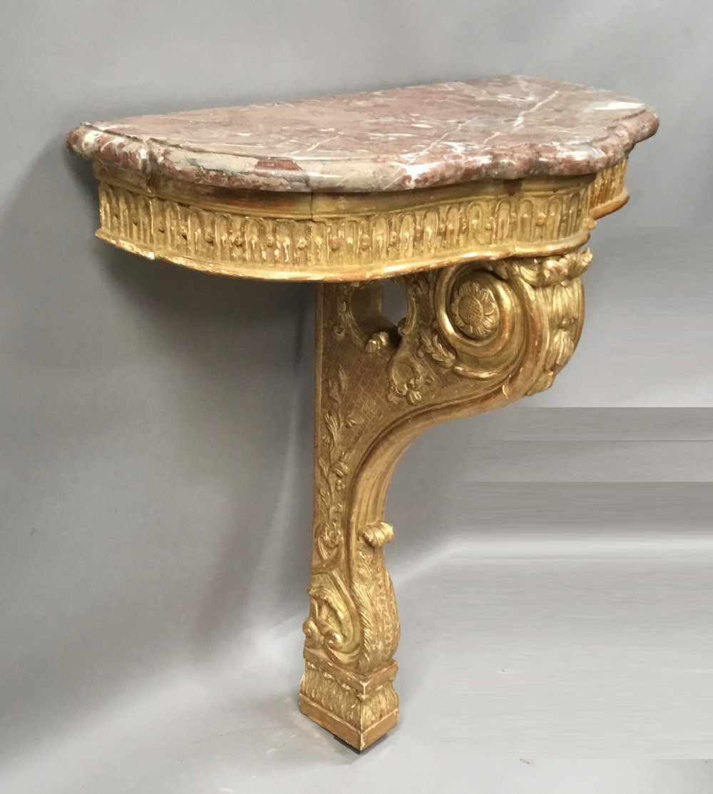 A 19th-century French Louis XV style wall-mounted giltwood console table featuring a carved single scroll leg and a shaped pink marble top.