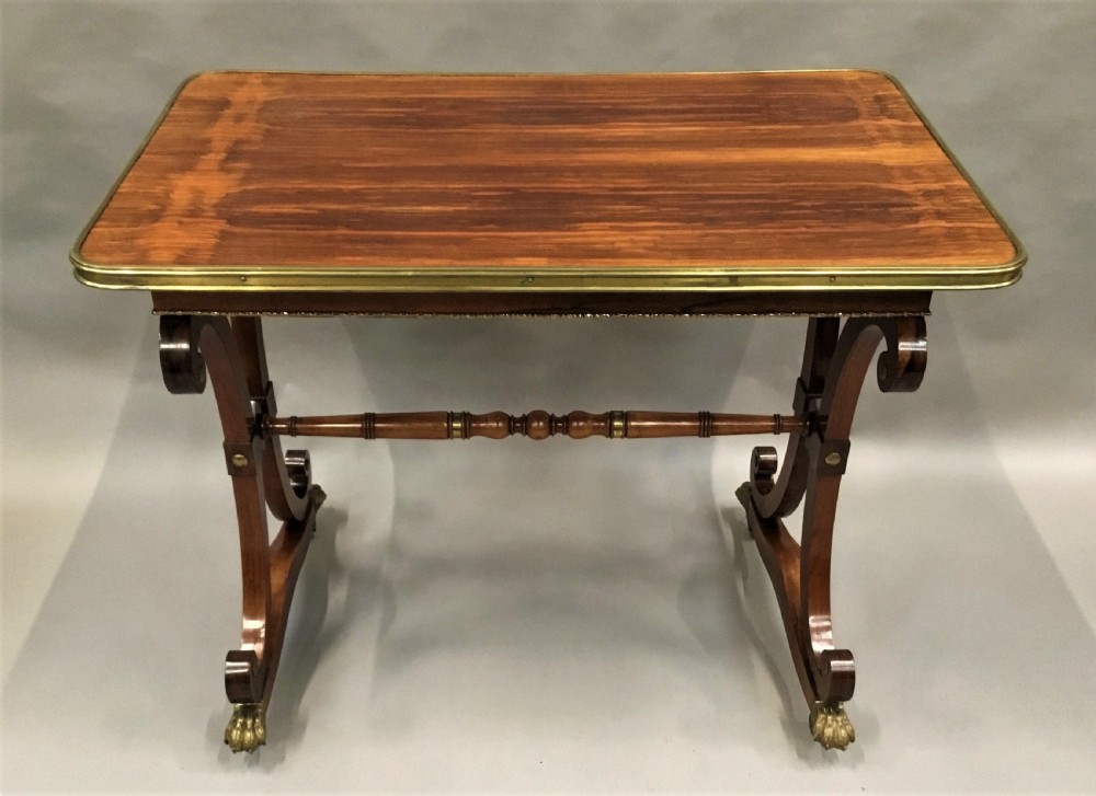 A Regency rosewood centre table featuring a rectangular brass-rimmed top supported by curved double-scroll legs with a turned stretcher and brass paw feet. View II