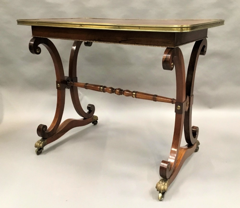 A Regency rosewood centre table featuring a rectangular brass-rimmed top supported by curved double-scroll legs with a turned stretcher and brass paw feet. View IV