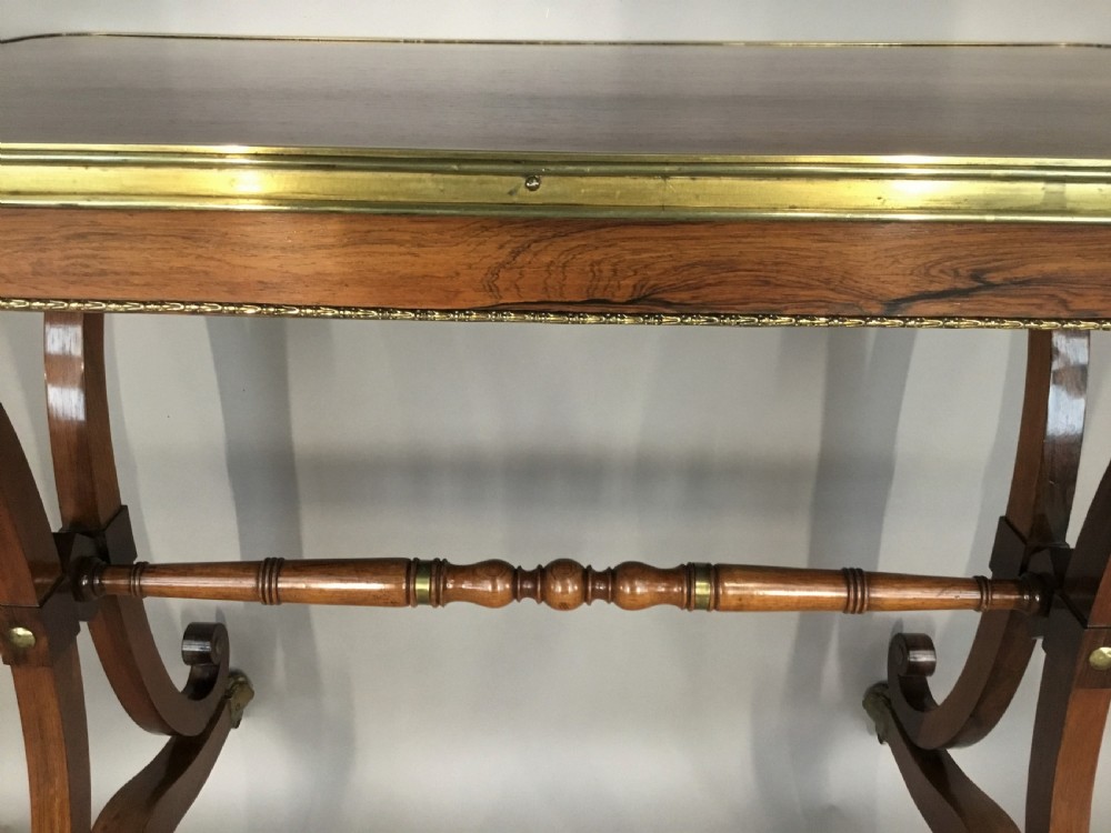 A Regency rosewood centre table featuring a rectangular brass-rimmed top supported by curved double-scroll legs with a turned stretcher and brass paw feet. View V