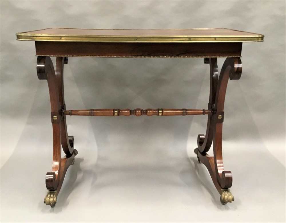A Regency rosewood centre table featuring a rectangular brass-rimmed top supported by curved double-scroll legs with a turned stretcher and brass paw feet. View VI