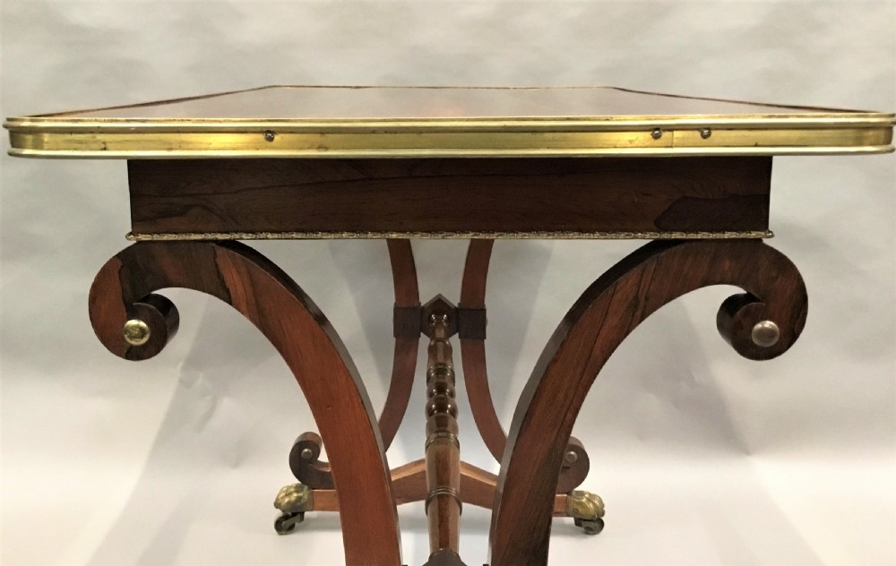 A Regency rosewood centre table featuring a rectangular brass-rimmed top supported by curved double-scroll legs with a turned stretcher and brass paw feet. View XIII