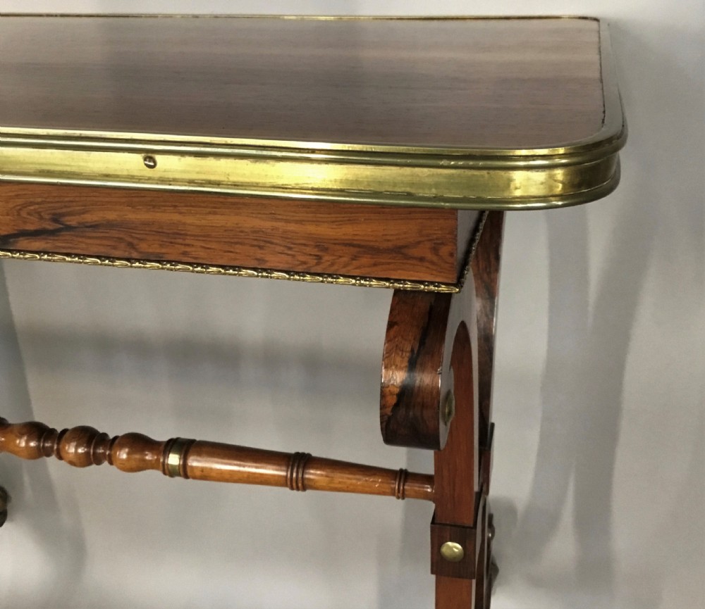 A Regency rosewood centre table featuring a rectangular brass-rimmed top supported by curved double-scroll legs with a turned stretcher and brass paw feet. View XIV