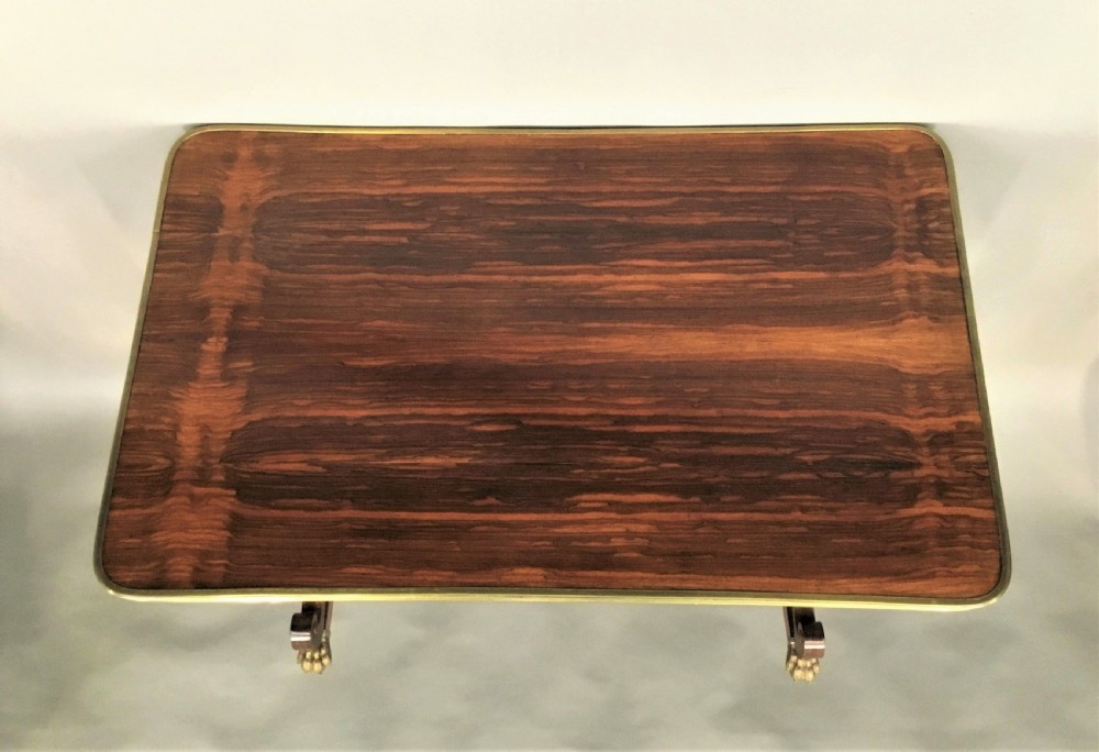 A Regency rosewood centre table featuring a rectangular brass-rimmed top supported by curved double-scroll legs with a turned stretcher and brass paw feet. View XVII