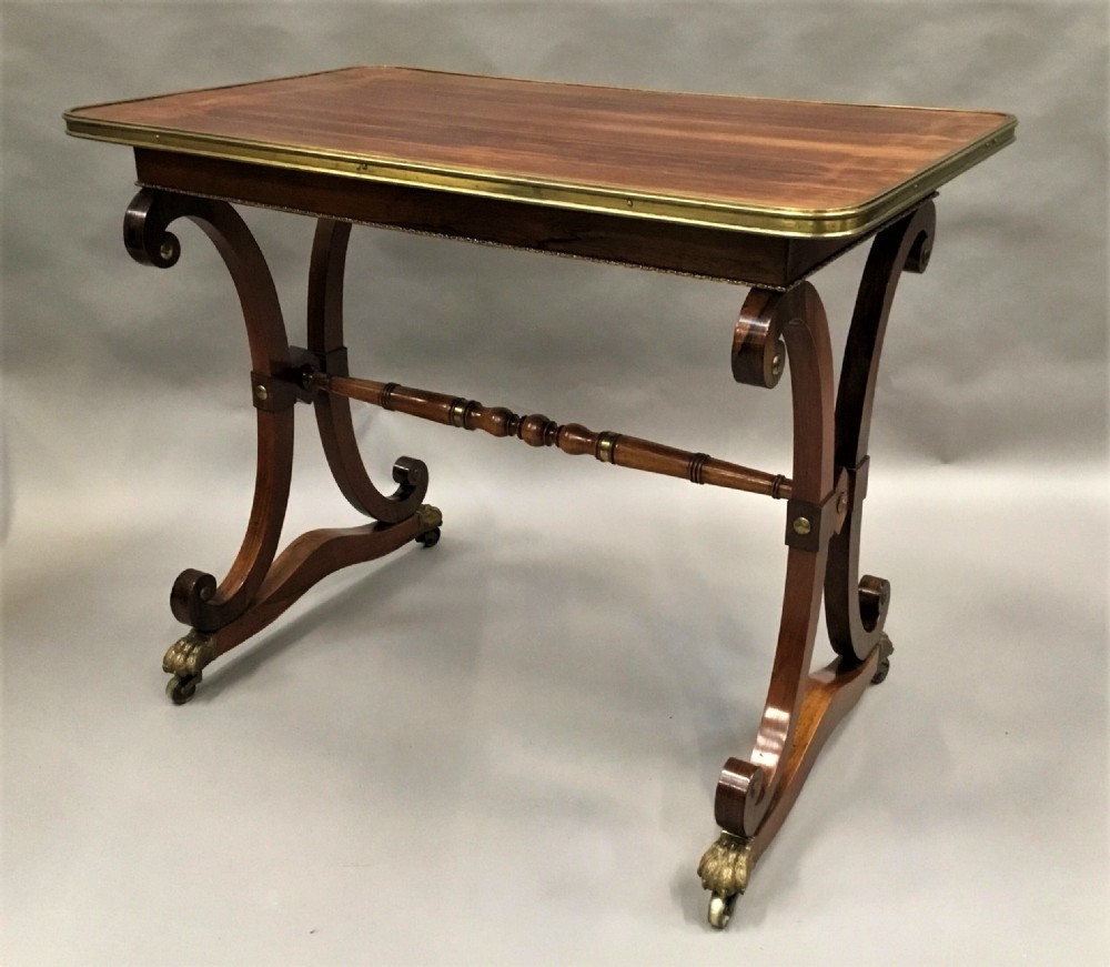 A Regency rosewood centre table featuring a rectangular brass-rimmed top supported by curved double-scroll legs with a turned stretcher and brass paw feet. View XIX