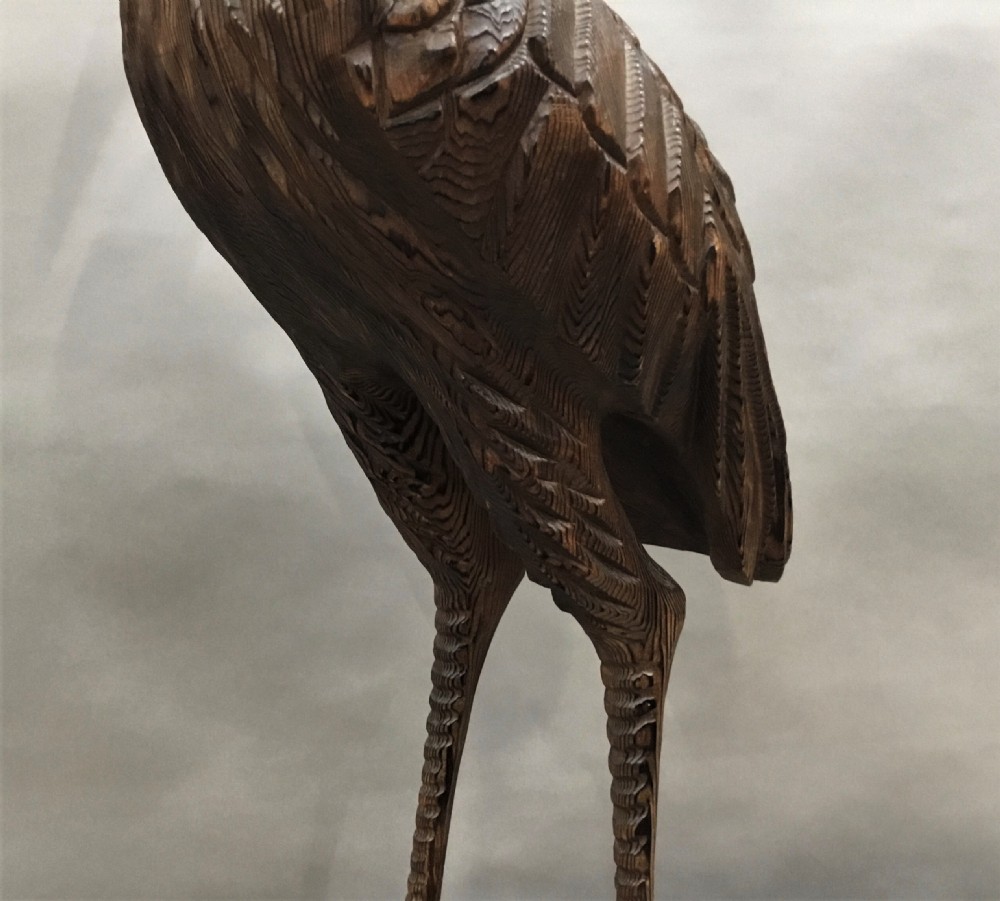 A nineteenth-century carved pine sculpture of a standing heron with detailed feather carving mounted on a sculpted wooden base. View XX