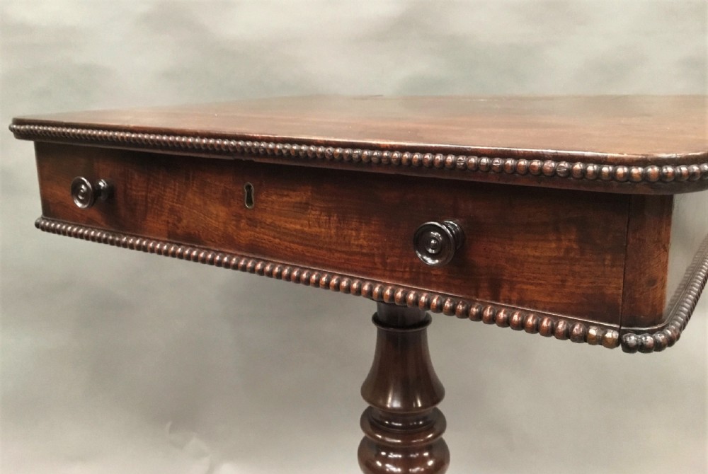 A Regency mahogany writing table featuring an adjustable hinged top, a single drawer with turned knobs, a turned central pedestal, and reeded tripod legs ending in brass castors. View VI