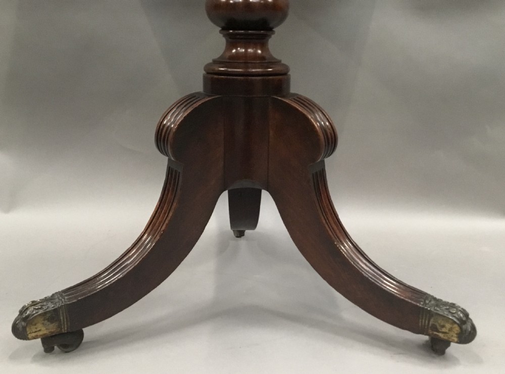 A Regency mahogany writing table featuring an adjustable hinged top, a single drawer with turned knobs, a turned central pedestal, and reeded tripod legs ending in brass castors. View VII