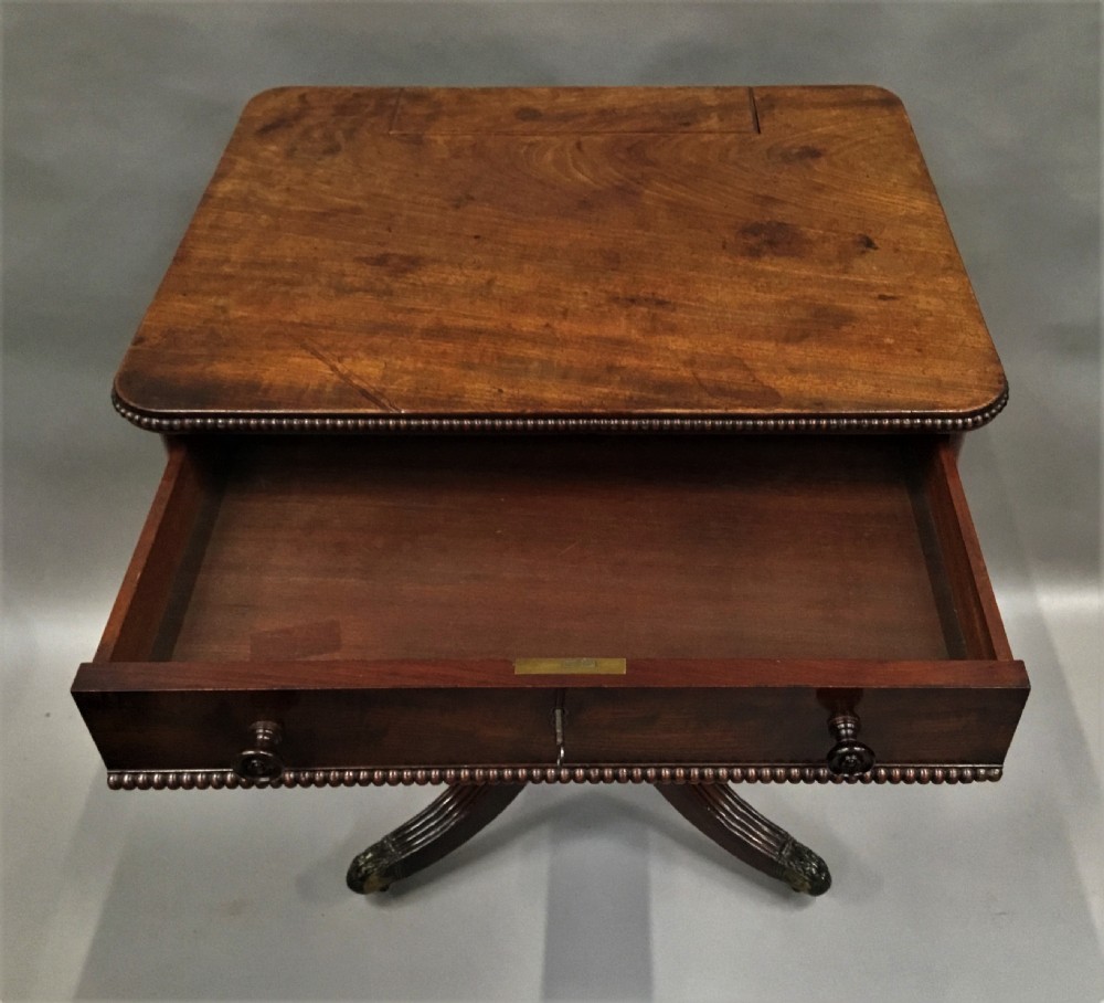 A Regency mahogany writing table featuring an adjustable hinged top, a single drawer with turned knobs, a turned central pedestal, and reeded tripod legs ending in brass castors. View VIII