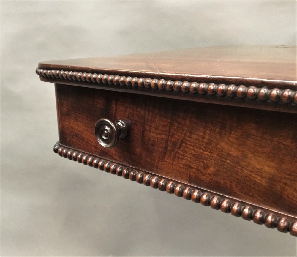 A Regency mahogany writing table featuring an adjustable hinged top, a single drawer with turned knobs, a turned central pedestal, and reeded tripod legs ending in brass castors. View X