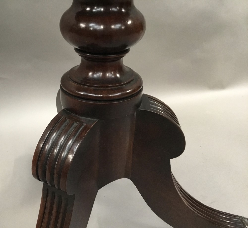 A Regency mahogany writing table featuring an adjustable hinged top, a single drawer with turned knobs, a turned central pedestal, and reeded tripod legs ending in brass castors. View XIV