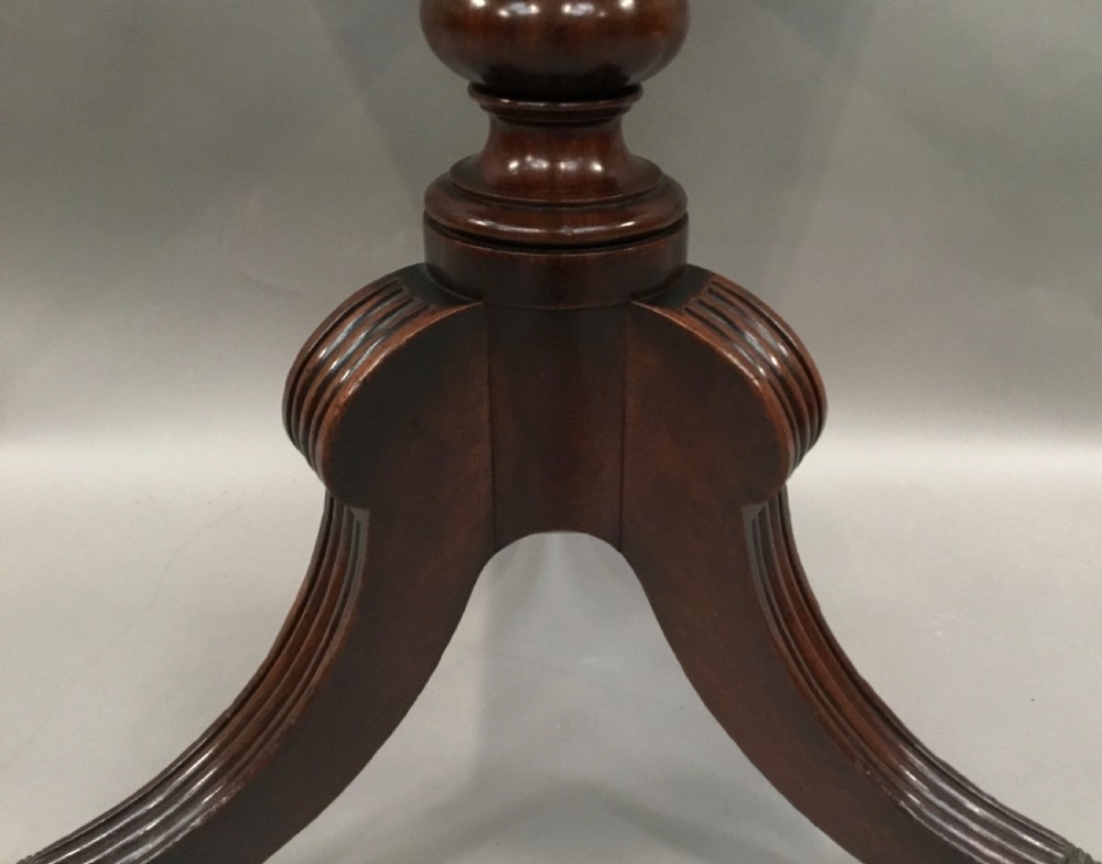A Regency mahogany writing table featuring an adjustable hinged top, a single drawer with turned knobs, a turned central pedestal, and reeded tripod legs ending in brass castors. View XVI